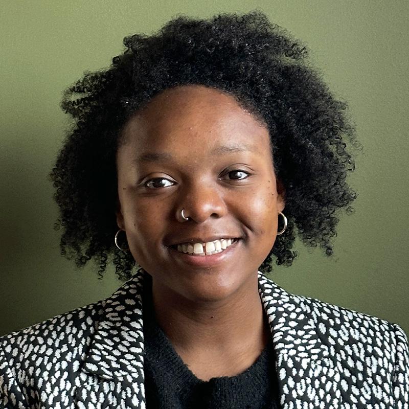 Headshot of JahAsia Jacobs, who is smiling and has short black curly hair. She wears a black and white spotted jacket.