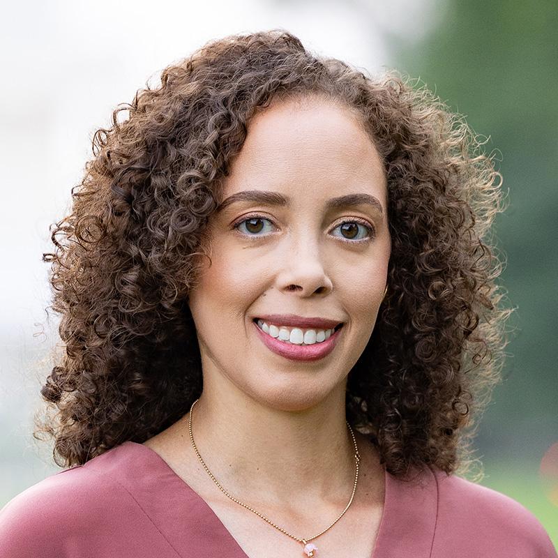 Headshot of Carla Burns, who is smiling and has shoulder length brown curly hair.