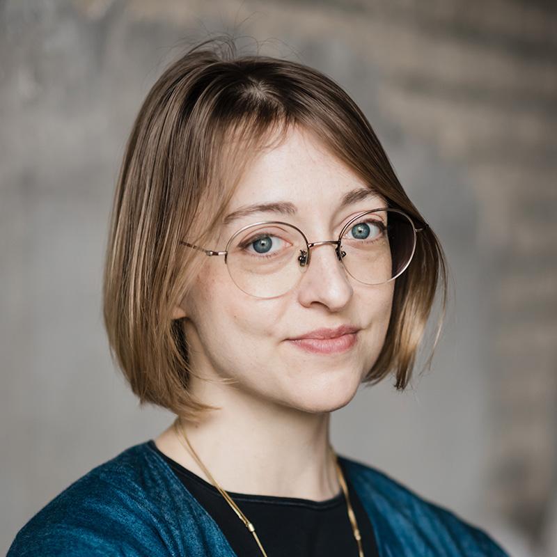 Headshot of Emily Owens, who is slightly smiling. She wears round glasses and has short blonde hair.