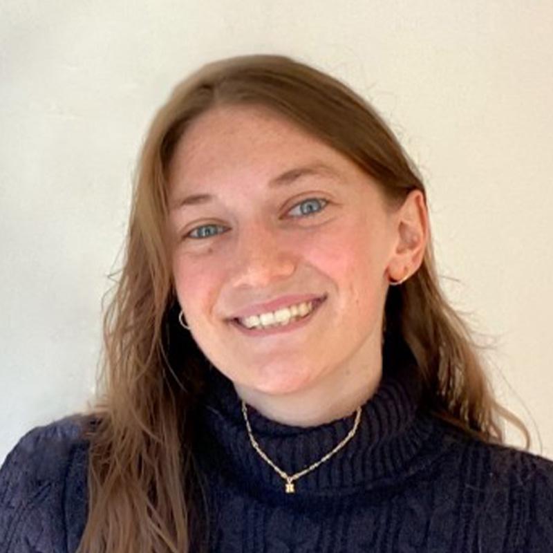 Headshot of Hannah Madden, who is smiling and has long light brown hair. She wears a black turtleneck.