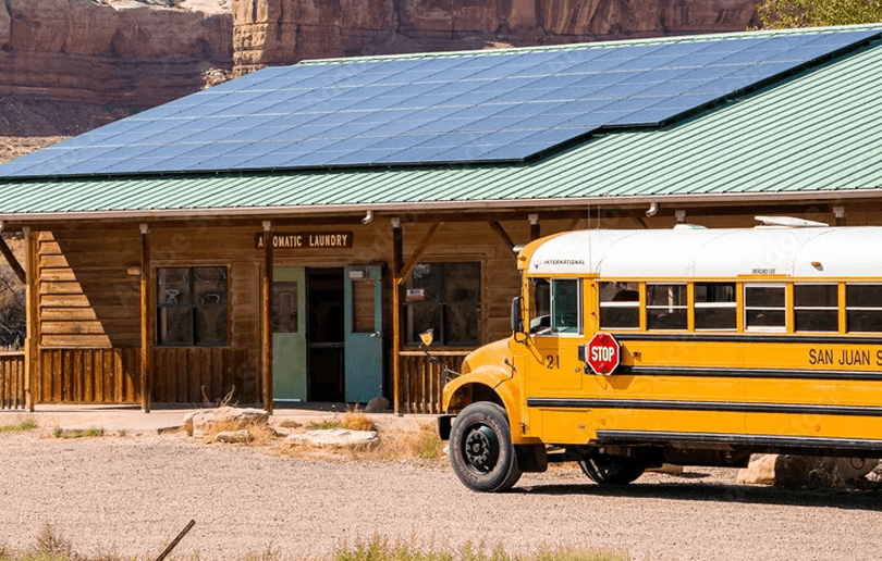 Yellow school bus in front of a wooden school building with solar panels on its roof