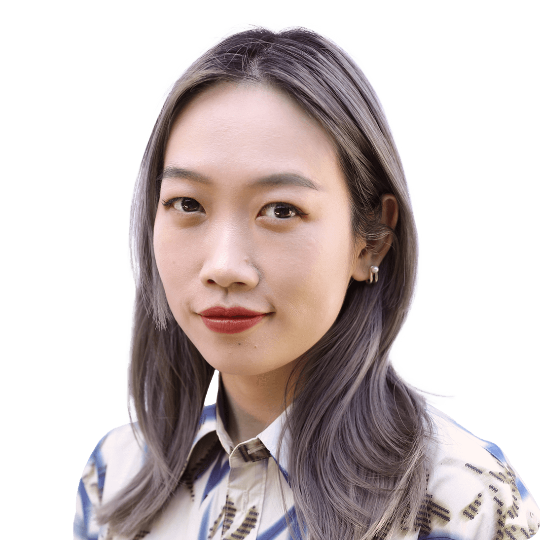 Headshot of Chell who smiles with her mouth closed and is looking toward the camera. she has shoulder length dyed grey hair and wears a printed collared long sleeve shirt.